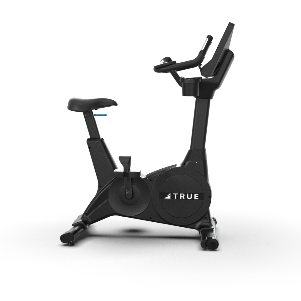 A stationary exercise bike with a digital display, adjustable seat, and pedals. The frame is black, and the brand name TRUE is visible on the side of the bike’s flywheel cover.