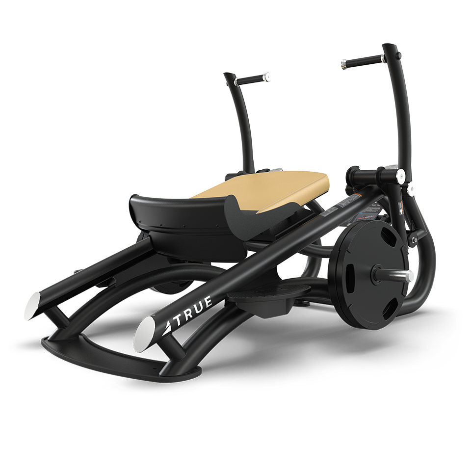 Black and tan gym equipment with handlebars, padded seat, and weight plates on the side, designed for lower body and leg exercises. The brand TRUE is visible on the frame.